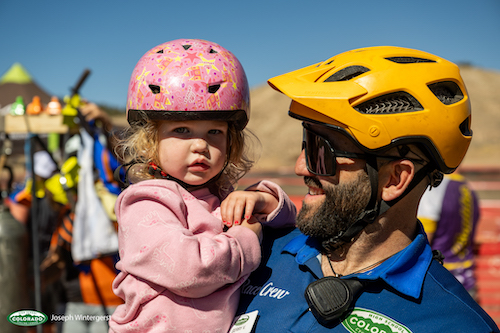Race crew holds toddler with bike helmets on in Eagle, CO